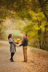 Obraz premium Couple weared in autumn-style clothes (oranfe scarf and vest) stay in the autumn landscape. Alley covered with yellow foliage. Autumn walk outdoors. Two lovers in autumn park. Romantic dating