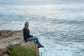 Mujer sentada en roca mirando el mar.