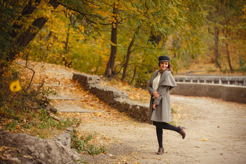 Fototapeta premium Autumn mood. Romantic woman weared in beige cloak walk in a park on background of beautifull autumn leaves. Smile. fall coming. Brown-haired girl with long hairs.