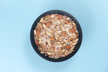 A fresh granola with dried and candied nuts and fruits in black bowl on blue bakground.
