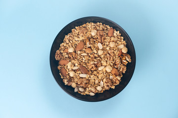 A fresh granola with dried and candied nuts and fruits in black bowl on blue bakground.
