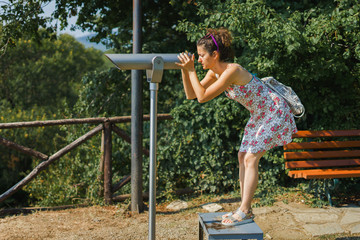 Young woman tourist in summer dress using monocular telescope binoculars to watch the scene from the mountain at the Aristotle's park at Stagira Greece in autumn