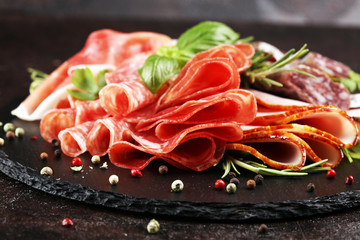 Marble cutting board with prosciutto, bacon, salami and sausages on wooden background. Rustic Meat...