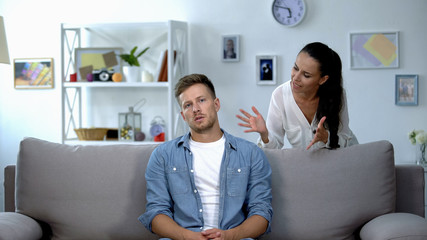 Phlegmatic man sitting on sofa listening nervous wife shouting, aggression