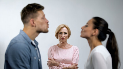 Displeased mother with hands crossed looking at young couple preparing to kiss