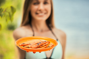 Roasted carrots on a bright orange plate holded by a young girl in swimsuit.