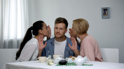Irritated man listening wife and mother-in-law whispering on ear, problems