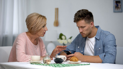 Worried mother talking to infantile adult son playing video games on smartphone