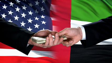 USA and UAE officials hands exchanging money on flag background, partnership