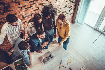 Group of young modern people in smart casual wear having a brainstorm meeting while standing behind...