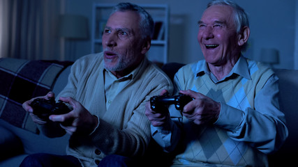 Excited retired men playing video game at night together, friendship connection