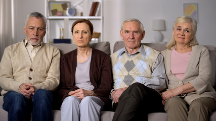 Obraz premium Upset senior friends sitting sofa looking camera, social problems, retirement