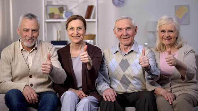 Smiling elderly people showing thumbs up on camera, social reform improvement