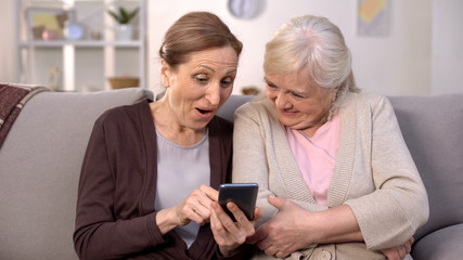Happy aged friends watching online video on smartphone, modern technology, app