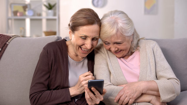 Cheerful old women watching photos on smartphone laughing, good memories, fun