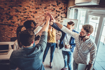 Successful team of young professionals celebrating achievement in work project giving high-five to each other in office