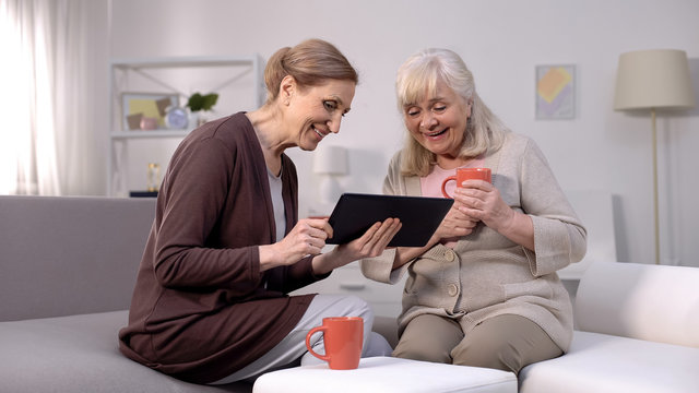 Cheerful mature women watching tablet video, shopping application, technology