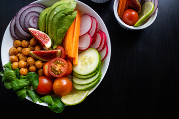 Vegetarian Buddha bowl on a white plate with figs, avocado, chickpeas and other fresh vegetables. Top view.