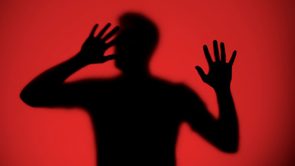 Desperate male silhouette trying to escape from captivity, red background