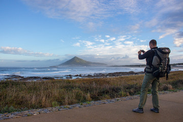 Man takes picture at seaside in Portugal. Pilgrim with backpack on Camino de Santiago road. Aerial view of mountain and ocean in the morning. Cloudy sunrise on Atlantic ocean coast, Portugal. 