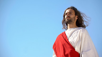 Serious Jesus Christ in white robe looking at humanity from heaven, religion