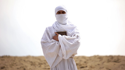 Bedouin in white robe holding Koran, preacher of Islamic faith and teachings