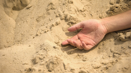 Male hand lying lifeless on sand, death of thirst in sahara, lack of water