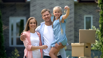 Moving in, happy family smiling, daughter showing house keys, social mortgage
