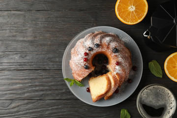 Cake with powdered sugar, berries and mint on wooden background, top view