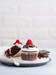 Chocolate muffins with a cup of coffee and fresh raspberries on the table, light background with space text. Selective focus.
