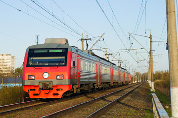Fototapeta na wymiar The red electric train travels along the railway lines towards the summer. Suburban passenger rail service.