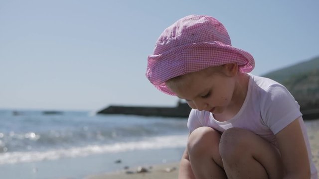 Little cute girl playing with sand on the beach by the sea.