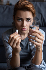 selective focus of sick woman holding pill and glass of water