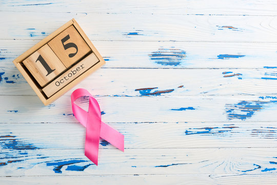 Pink ribbon and wooden cube calendar set for October 15 on a wooden table. Breast Cancer Awareness Month