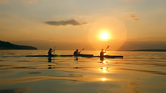 Boaters are kayaking at sunset in a side view