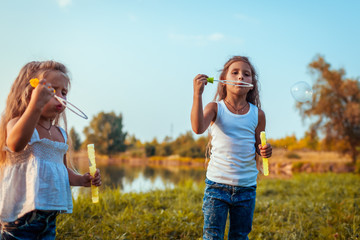 Girls blowing soap bubbles in summer park by river. Kids having fun outdoors. Games for children