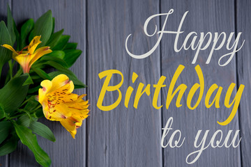 Greeting card with the inscription happy birthday. Congratulatory greeting to the girl, mother with flowers and a gift on a wooden background. Alstroemeria flowers