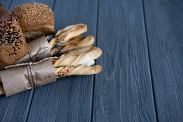 Brown bread, white bread with sesame seeds and bread sticks with sesame seeds, poppy seeds on a gray wooden background. Frame for text with bread for the design of the menu dish. Culinary background