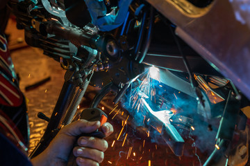 A man labor worker welding a motorcycle metal part indoor workshop with a lot of sparks