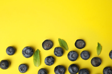 Tasty ripe blueberries and leaves on yellow background, flat lay with space for text