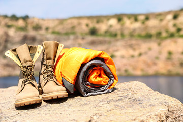 Sleeping bag and boots on cliff near lake. Space for text
