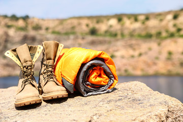 Obraz premium Sleeping bag and boots on cliff near lake. Space for text