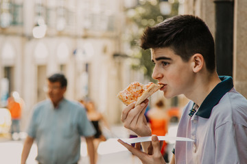 young man eating pizza by the city street