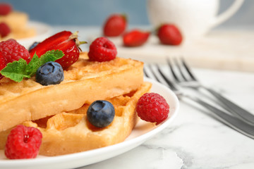 Delicious waffles with fresh berries served on white marble table, closeup