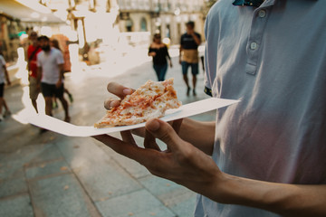 hands with slice of pizza on urban street outdoors