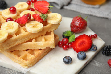 Board with delicious waffles and fresh berries on grey table, closeup, Space for text