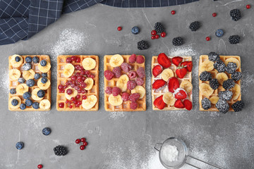 Flat lay composition with delicious waffles and fresh berries on grey table