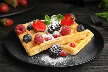 Delicious waffles with fresh berries served on black wooden table