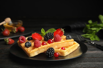 Delicious waffles with fresh berries served on black wooden table