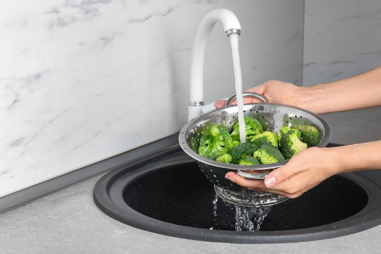 Woman washing fresh green broccoli in metal colander under tap water, closeup view. Space for text